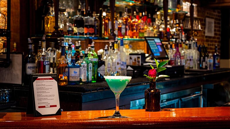 Green cocktail and flower vase on bar top